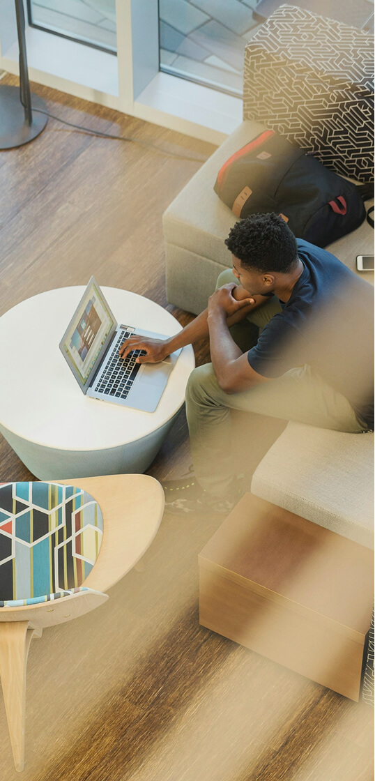 明るいラウンジスペースで、ソファに座りノートパソコンを操作している人物