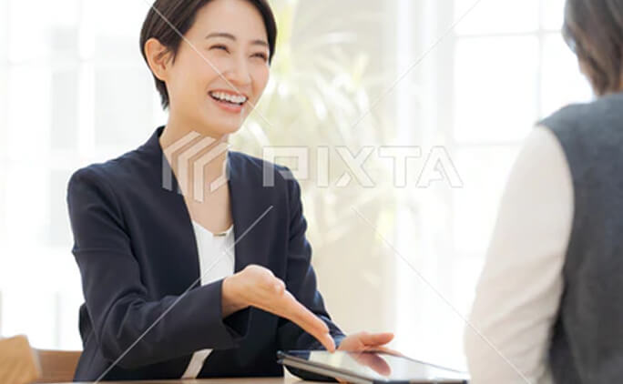 タブレットを使いながら来訪者に説明する女性社員